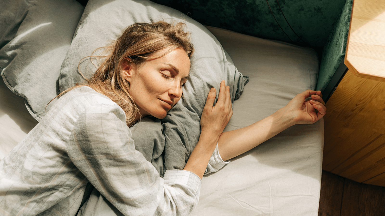 Frau liegt entspannt in einem Bett, umarmt ein Kissen und schläft mit einem leichten Lächeln – Symbol für guten Schlaf, gesunde Schlafgewohnheiten und Schlaftherapie in der Ergotherapie.