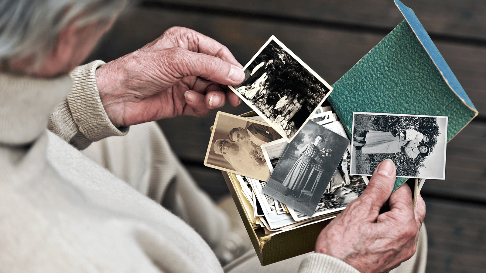 Ältere Person betrachtet eine Sammlung alter Schwarz-Weiß-Fotografien aus einer Erinnerungsbox – Symbol für Biografiearbeit, Demenztherapie oder das bewusste Erinnern an vergangene Lebensabschnitte.