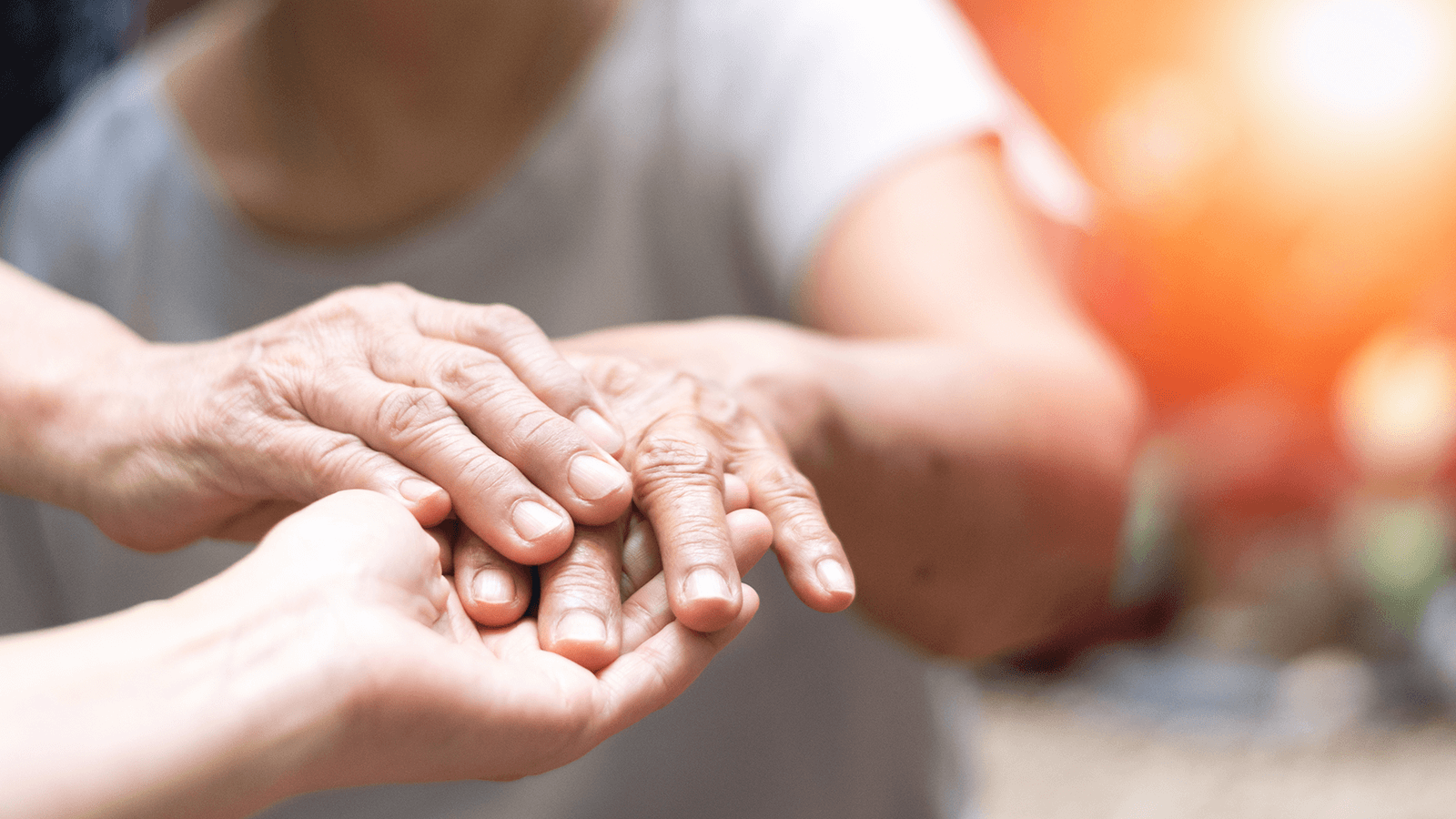 Zwei Menschenhände in Nahaufnahme: Eine jüngere Hand hält behutsam die Hand einer älteren Person mit sichtbaren Alterserscheinungen. Die Geste vermittelt Fürsorge, Unterstützung und Nähe. Im Hintergrund scheint warmes Sonnenlicht durch, wodurch eine hoffnungsvolle und positive Stimmung entsteht. Die Szene steht sinnbildlich für therapeutische Begleitung im Alter – etwa bei der Behandlung von Parkinson-Erkrankungen im Rahmen der Ergotherapie.