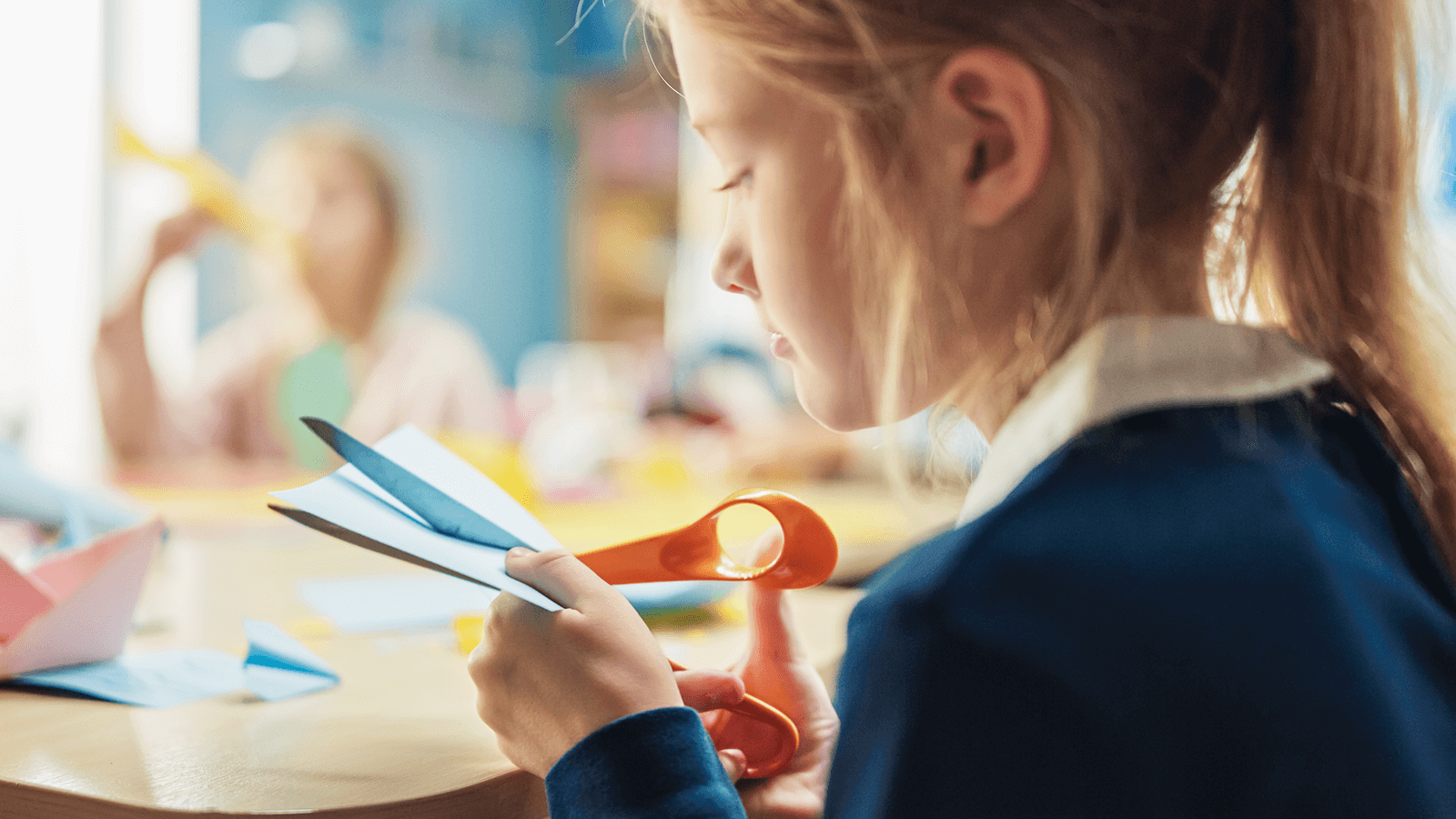 Junges Mädchen konzentriert sich beim Ausschneiden von farbigem Papier – Förderung der Feinmotorik und Konzentration, wie sie z. B. in der Ergotherapie für Kinder mit Schreib- oder Aufmerksamkeitsproblemen eingesetzt wird.