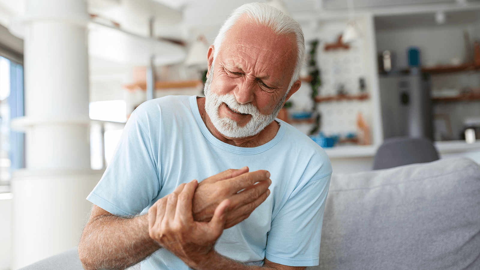 Älterer Mann mit weißem Bart hält sich unter sichtbarem Schmerz die Hand – Darstellung chronischer Beschwerden wie Arthrose, Rheuma oder Nervenschmerzen.